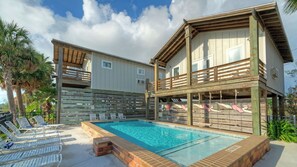 A two-story building with a swimming pool, lounge chairs, and a wooden deck.