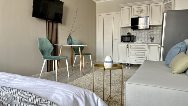 Een hotelkamer met een bed, een aan de muur bevestigde televisie, een eettafel met stoelen en een kitchenette met een magnetron en een koelkast.