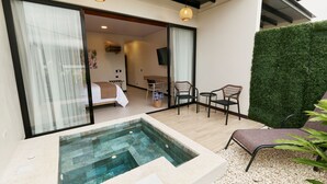 Et moderne hotelværelse med en glasindhegnet balkon, en lille pool og et siddeområde med stole og et bord.
