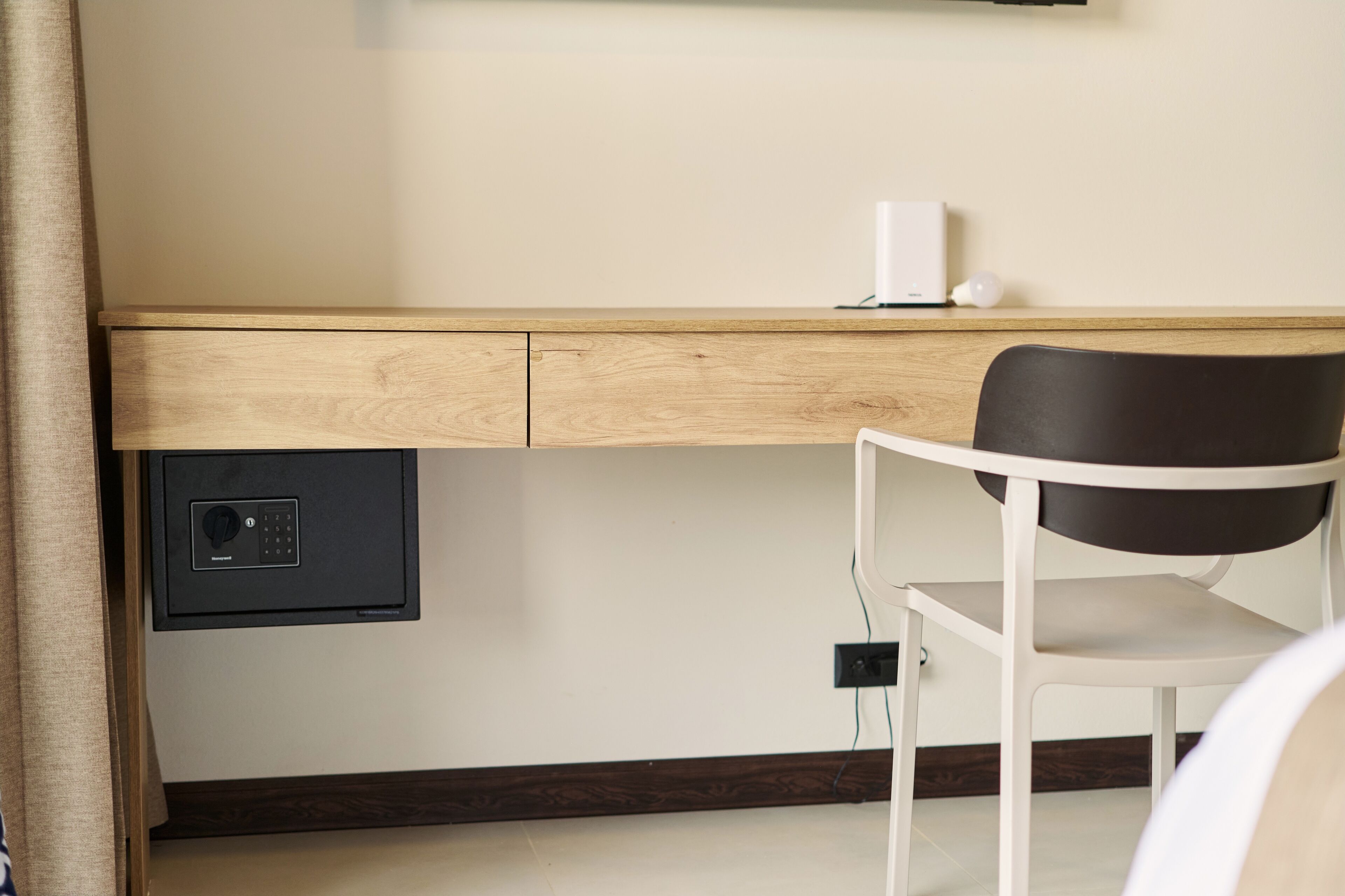 Een kamer met een houten bureau, een stoel, een kluisje en een stopcontact.