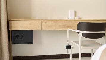 Een kamer met een houten bureau, een stoel, een kluisje en een stopcontact.