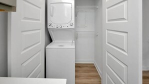 A laundry room with a washing machine and dryer, a metal rack, and a door leading to a closet. - Modern Escape Near Downtown Hotspots (Birmingham)