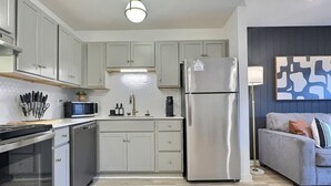 A modern kitchen with light grey cabinets, stainless steel appliances, and a grey sofa in the living area. - Modern Escape Near Downtown Hotspots (Birmingham)