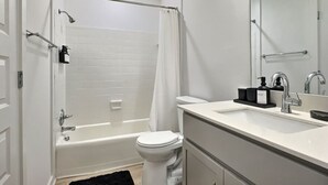 A modern bathroom with a bathtub, toilet, and sink. - Modern Escape Near Downtown Hotspots (Birmingham)
