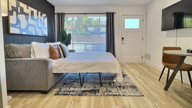A modern bedroom with a bed, a grey sofa, a dining table with chairs, and a TV on the wall. - Modern Escape Near Downtown Hotspots (Birmingham)