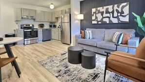 A modern kitchen with stainless steel appliances, a dining area with a round table, and a living room with a sofa and a large abstract painting on the wall. - Modern Escape Near Downtown Hotspots (Birmingham)