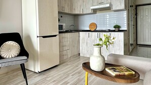 Cocina moderna con refrigerador, microondas y estufa integrados. Hay un comedor con una silla y una mesa pequeña con un florero y un libro.