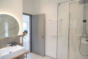 Un baño moderno con un espejo grande, un lavamanos y una ducha con cerramiento de vidrio.