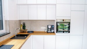 A modern kitchen with white cabinets, a wooden countertop, a built-in oven, and a coffee maker.