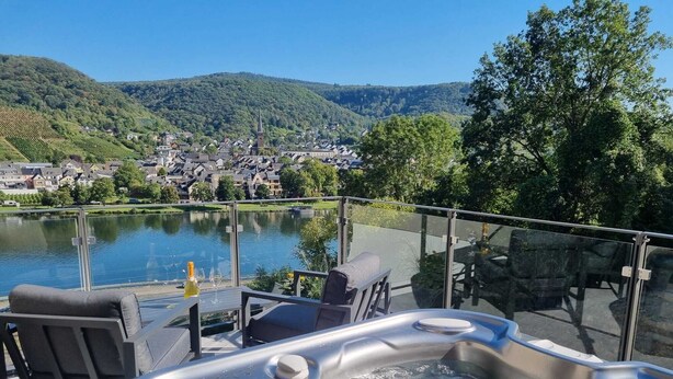A hot tub with a glass railing overlooking a lake and a town.