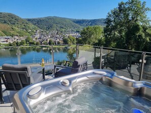 Un jacuzzi con barandilla de vidrio con vista a un lago y un pueblo.