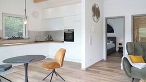 A modern kitchen with white cabinets, a built-in oven, and a dining area with a table and chairs.