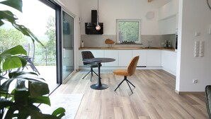 A modern kitchen with a dining area, large windows, and a view of greenery.