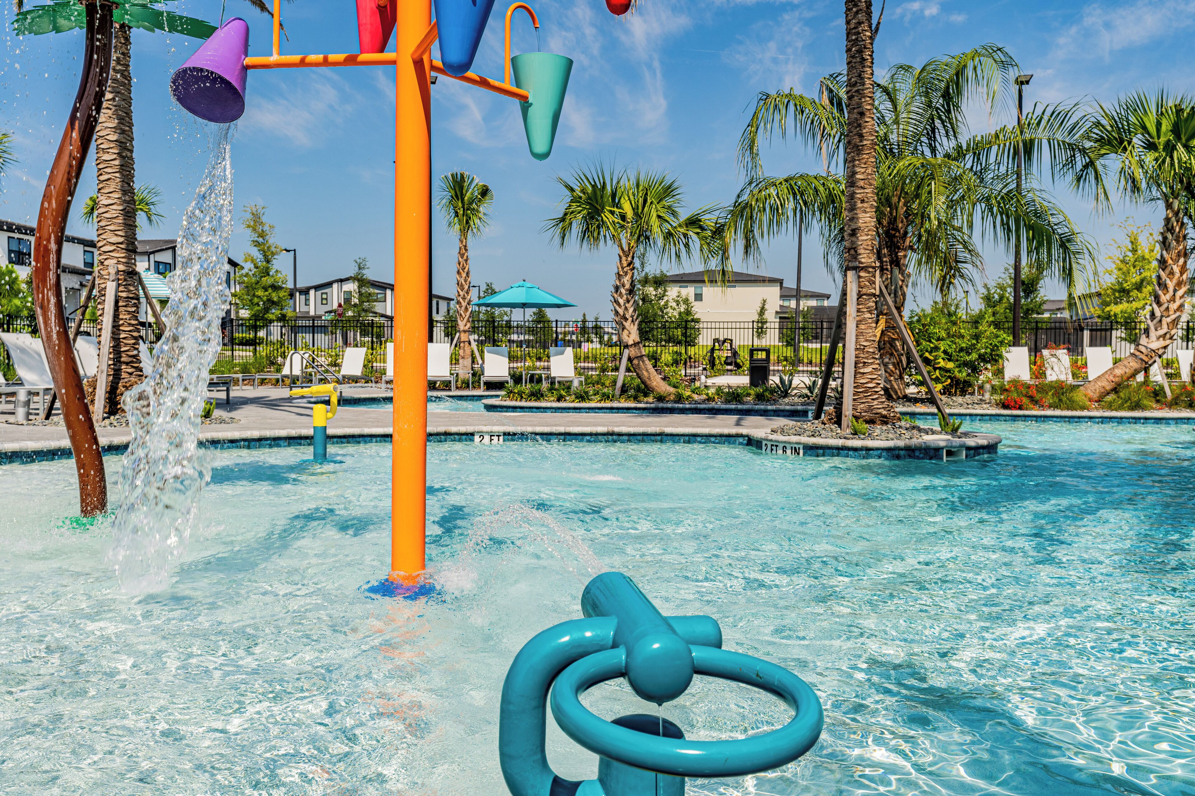 A water park with a pool, palm trees, and a colorful water play structure.