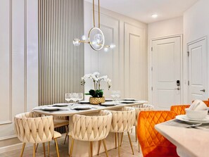 A dining area with a round table set for four, surrounded by six upholstered chairs with a tufted design.