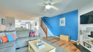 A living room with a grey sofa, a coffee table, a ceiling fan, a staircase, and a blue accent wall. - Spacious, family friendly 4-bedroom condo with pool in charming Dewey Beach!! (Dewey Beach)