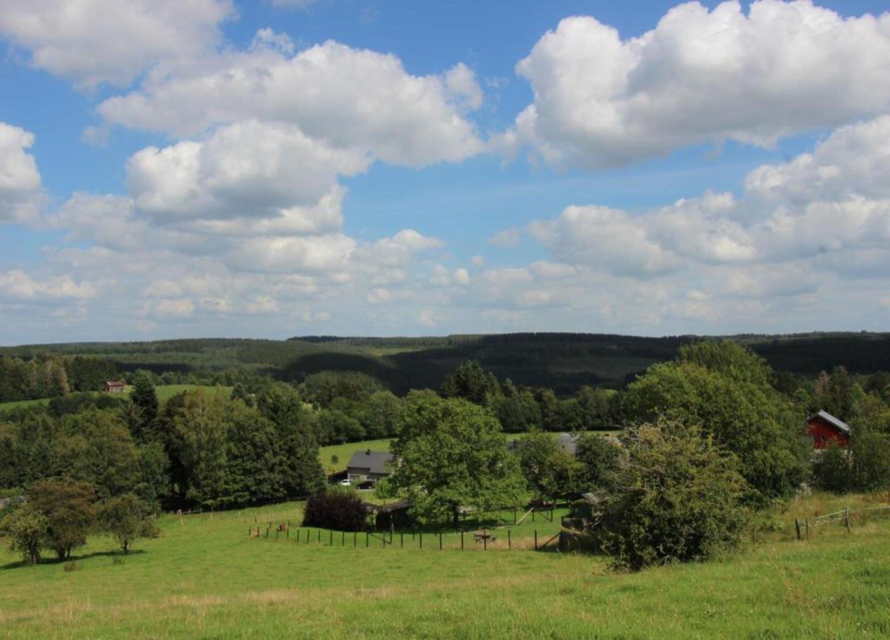 A rural landscape with rolling hills, scattered trees, and a few buildings.