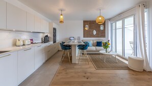 A modern kitchen with white cabinets, a dining area with a table and chairs, and a large window with curtains. - Ty Enogat- Proche de la plage, garage privé (Dinard)