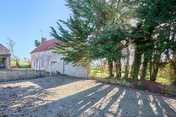 A gravel driveway leading to a stone building with a red roof, surrounded by trees and a playground.