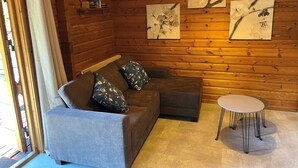 Una habitación acogedora con una pared de troncos de madera, un sofá gris con cojines florales, una pequeña mesa redonda y tres cuadros con motivos florales.