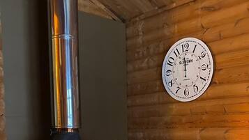 A wood-burning stove with a chimney, a clock on the wall, and a lantern on the floor.