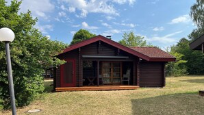 Una cabaña de madera pequeña con techo rojo, un porche y una puerta corrediza de vidrio.