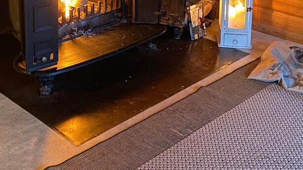 Una estufa de leña con fuego a la vista, un reloj en la pared y un farol en el suelo.