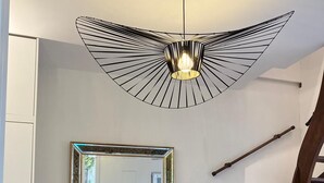 A dining area with a round wooden table, chairs, a wooden cabinet, a large mirror, and a modern pendant light.