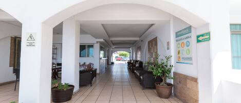 A corridor with potted plants, a sign indicating an evacuation route, and a sign with emergency contact information.