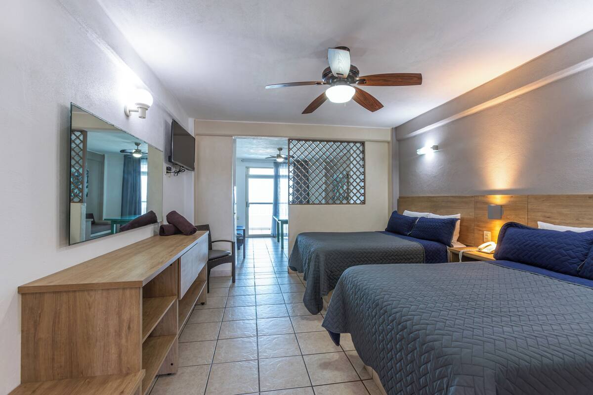 A hotel room with a bed, a desk, a chair, a TV, and a ceiling fan.