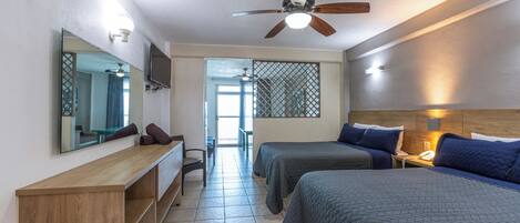 A hotel room with a bed, a desk, a chair, a TV, and a ceiling fan.