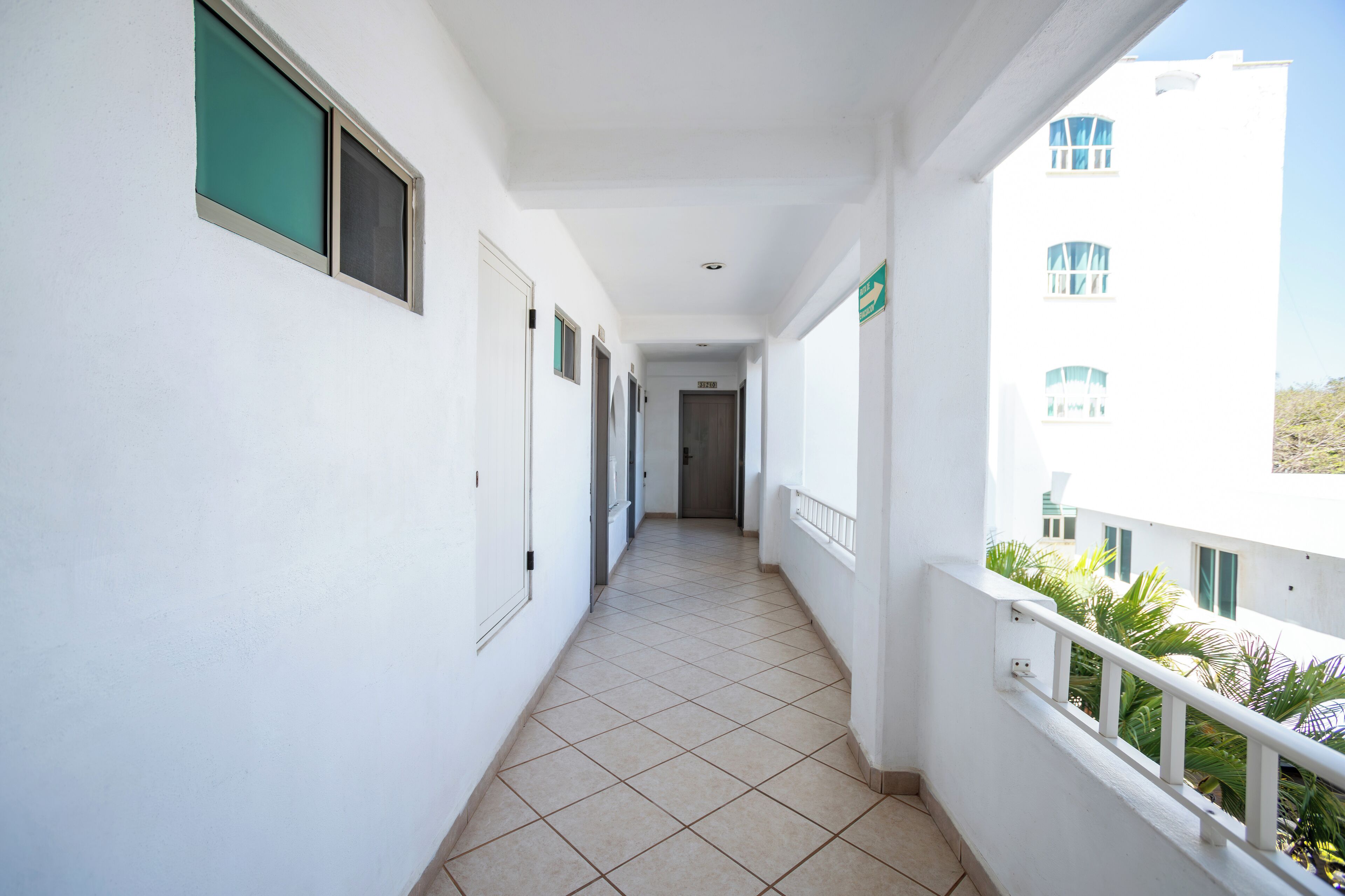 A corridor with white walls, a tiled floor, and a balcony with a railing.