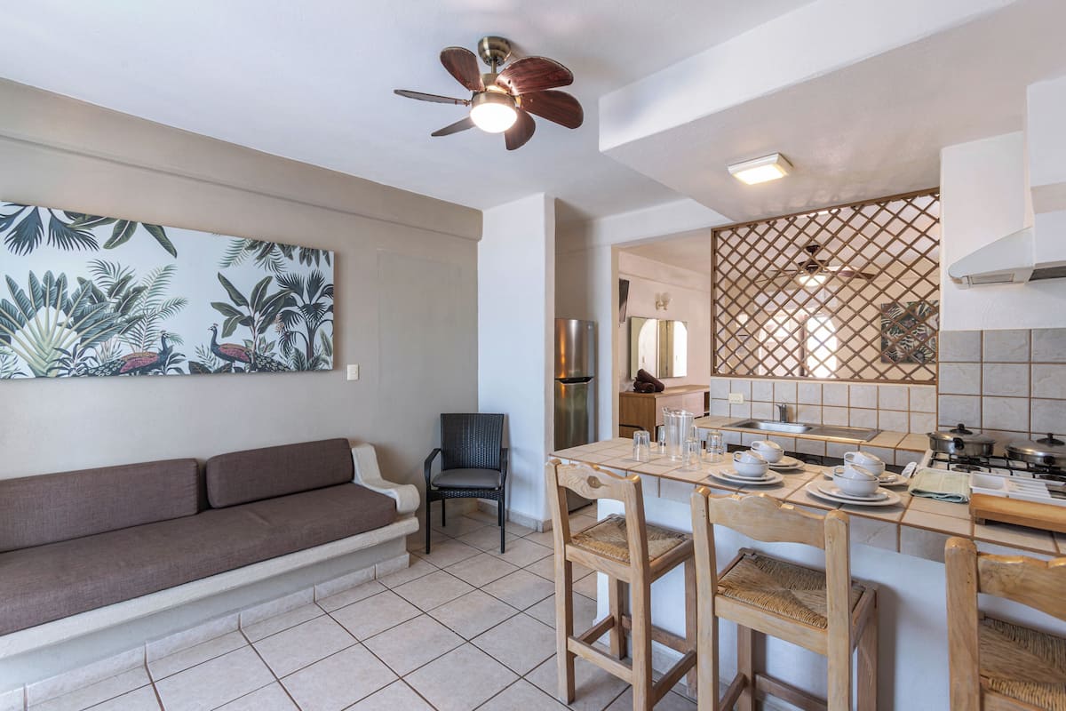 A modern kitchen with a dining area, a sofa, and a ceiling fan.
