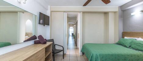 Un dormitorio con tocador de madera, cama verde, ventilador de techo y pasillo que conduce a otra habitación.