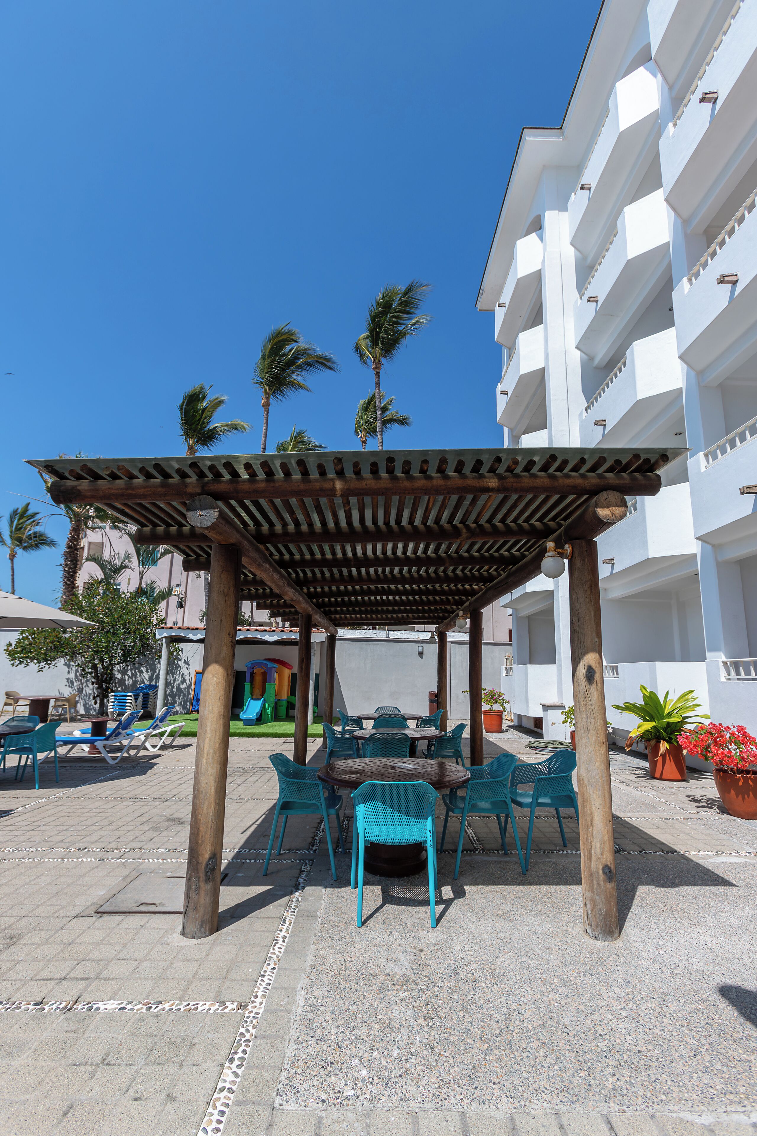 Un espacio de patio al aire libre con una pérgola de madera, sillas azules y una mesa.