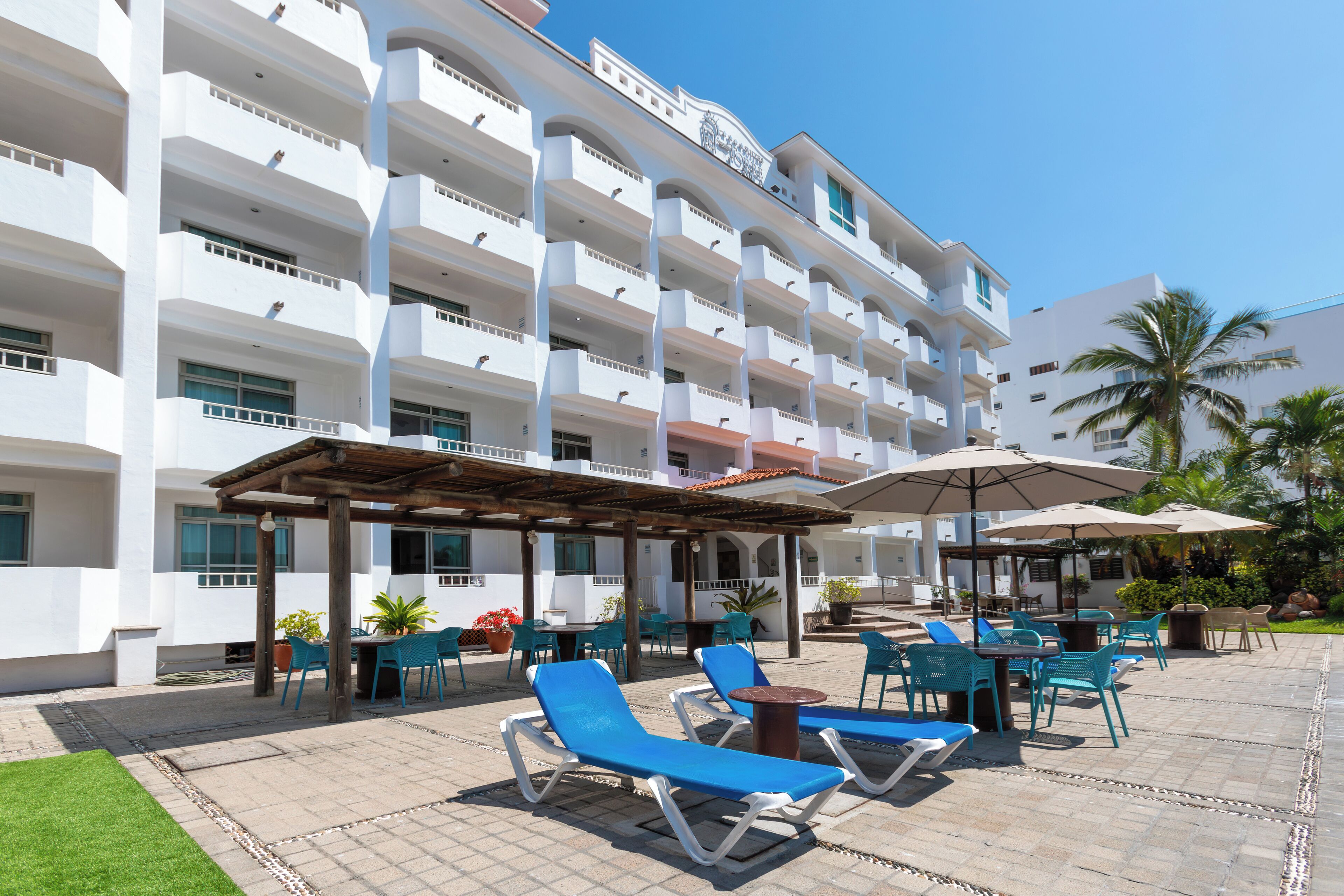 A hotel with multiple balconies, outdoor seating with umbrellas, and a pool area.