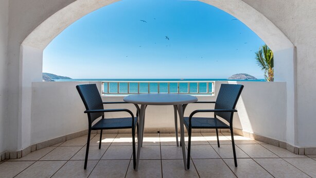 A balcony with a table and two chairs, overlooking a clear blue sea and a distant island. - Torreblanca Beach Hotel and Suites Guayabitos - Desayuno y Comida Incluido (Rincón de Guayabitos)