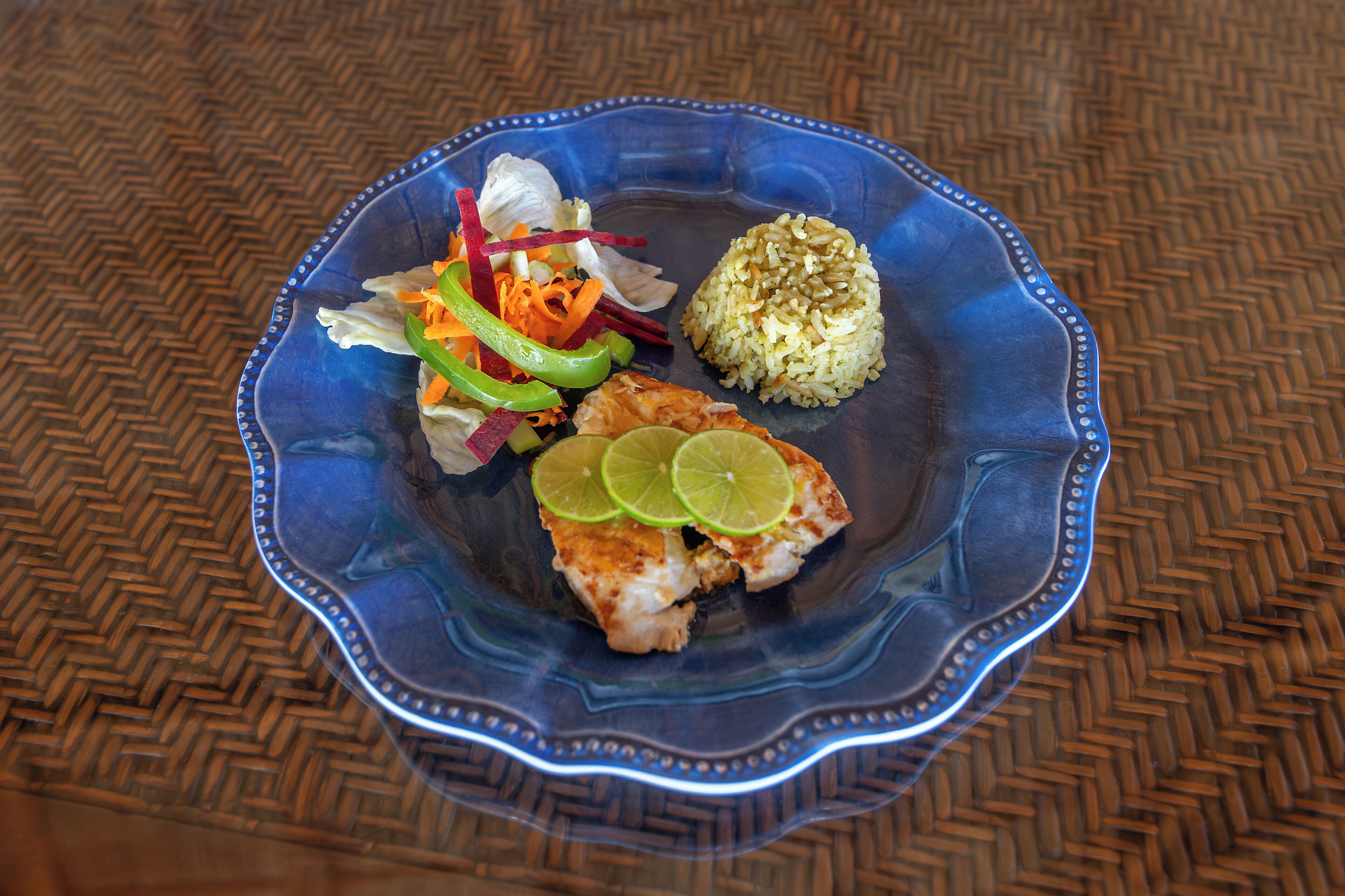 A blue plate with rice, a slice of meat topped with lime, and a salad with vegetables.