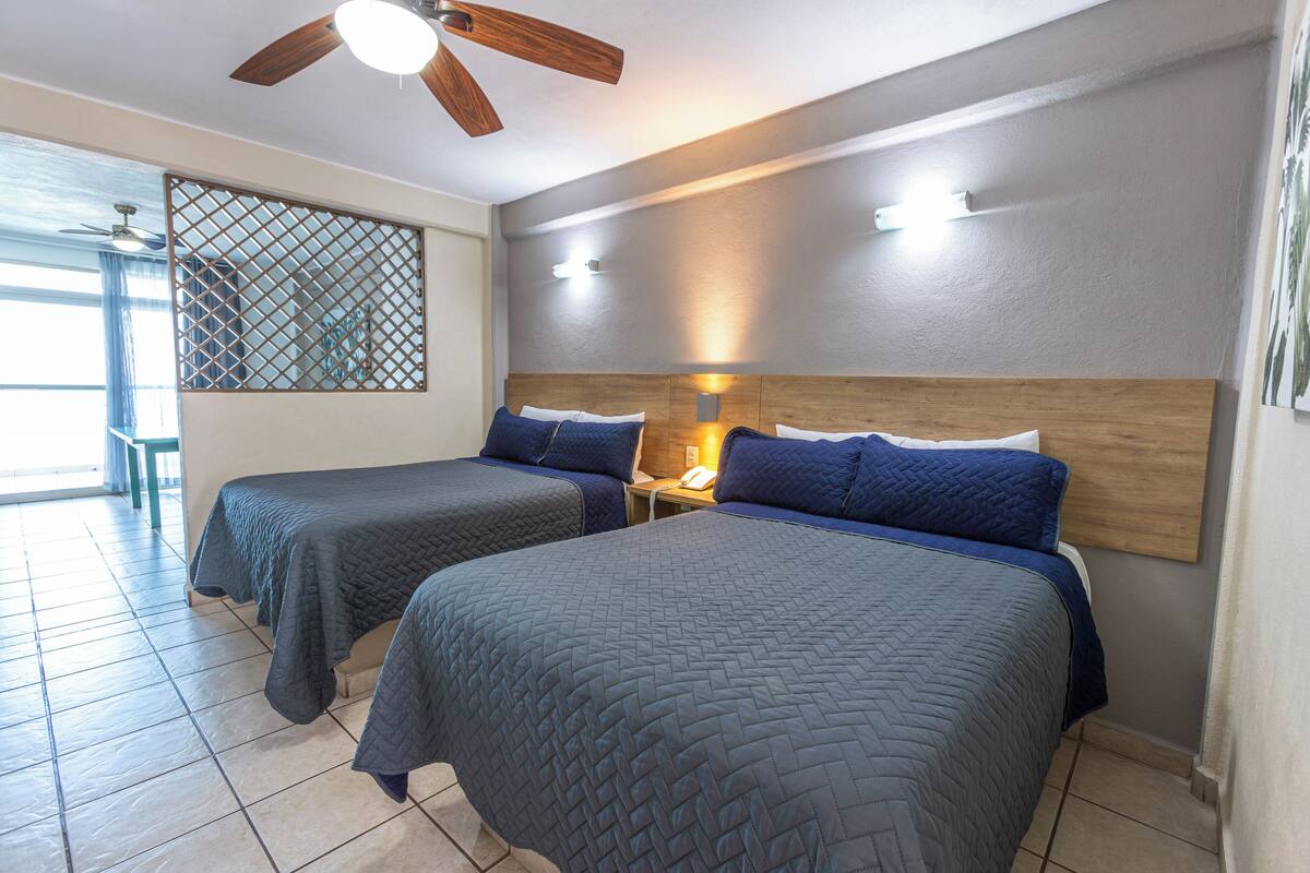 A hotel room with two beds, a ceiling fan, and a view of the outside.