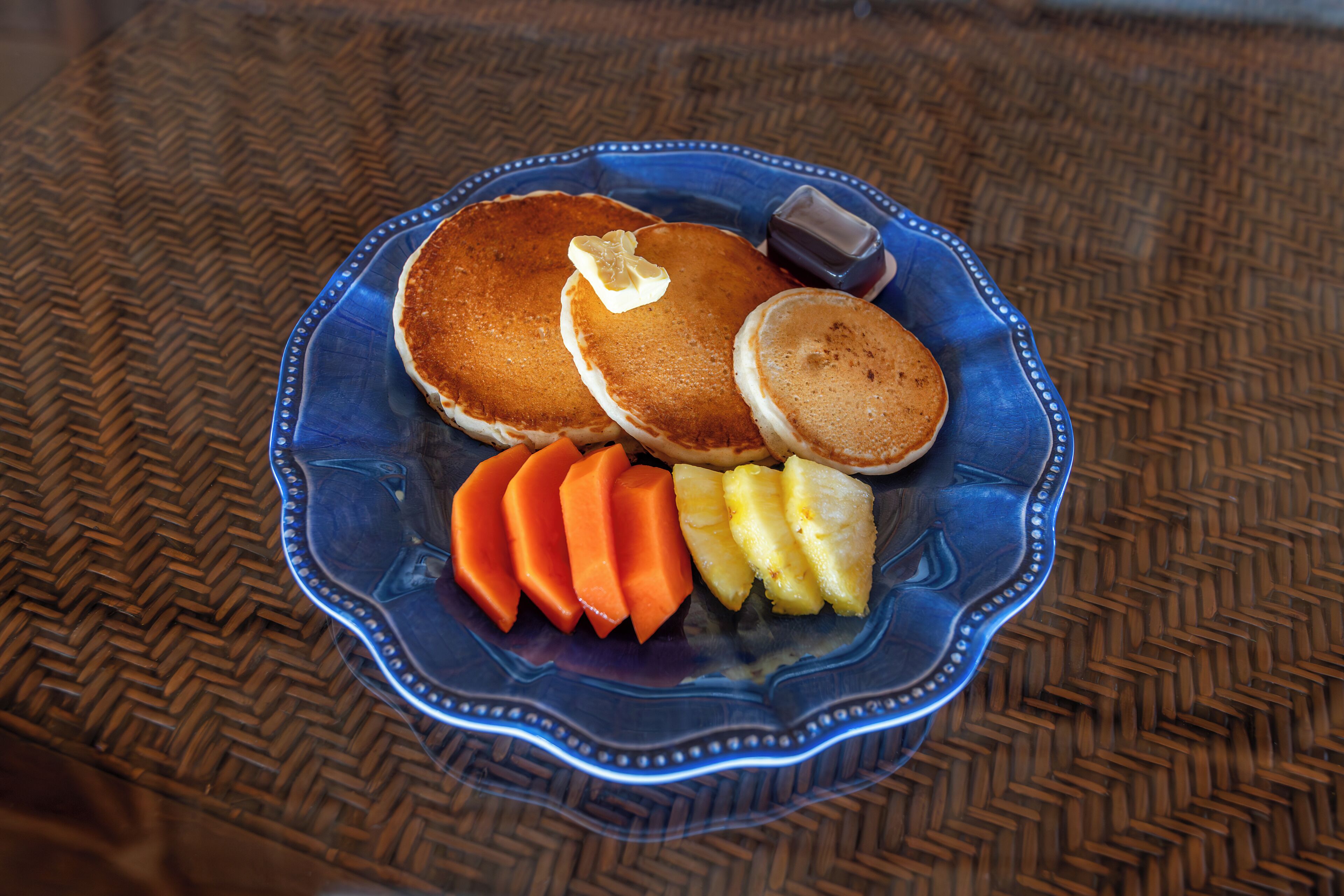 Une assiette de crêpes, de beurre, de sirop et de tranches d’ananas.