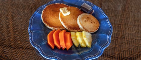 Un plato con tortitas, mantequilla, jarabe y rodajas de piña.