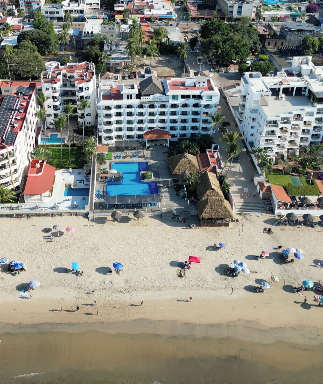 An aerial view of a resort with a swimming pool, beach, and multiple hotel buildings.