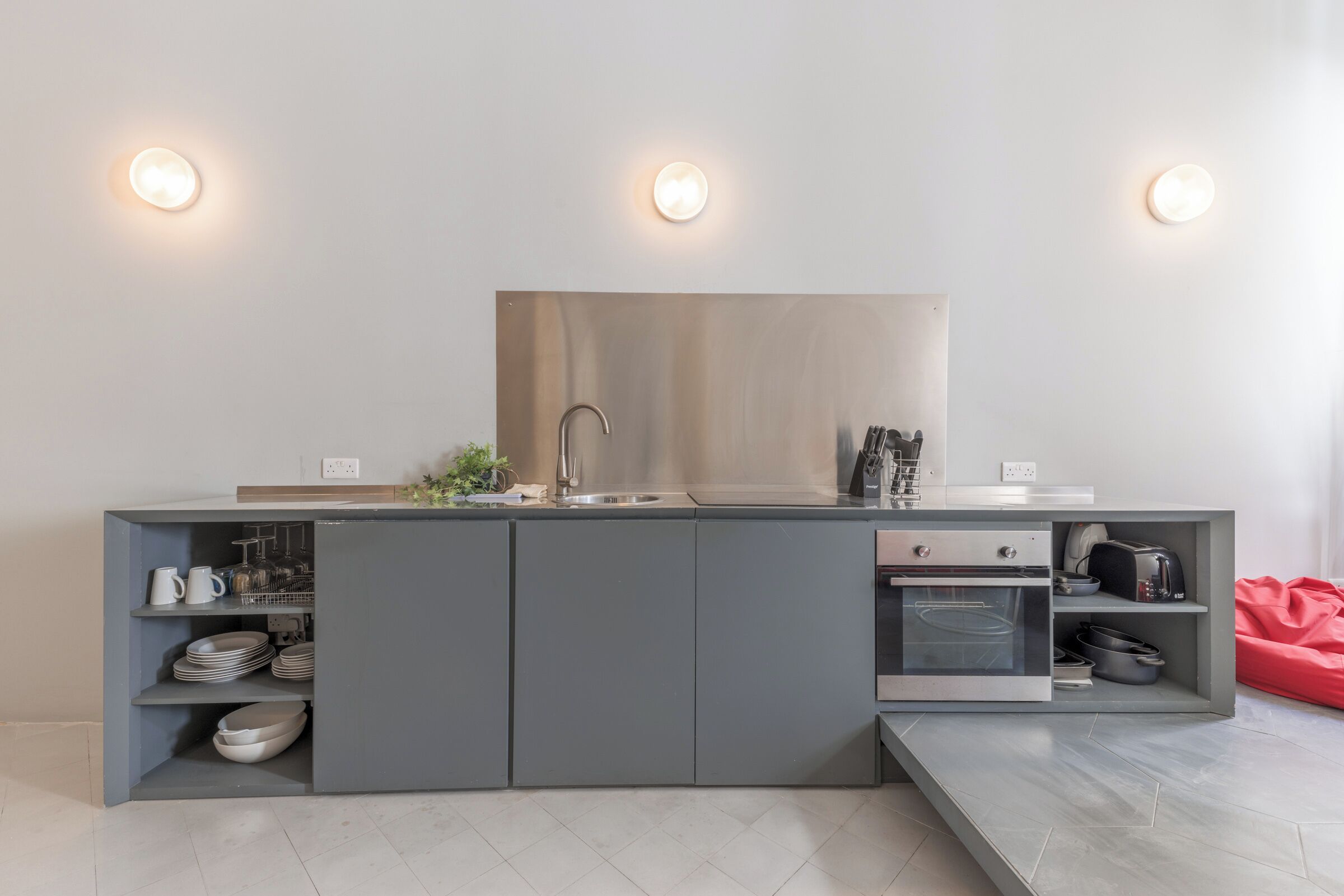 A modern kitchen with grey cabinetry, a built-in oven, and a stainless steel sink.