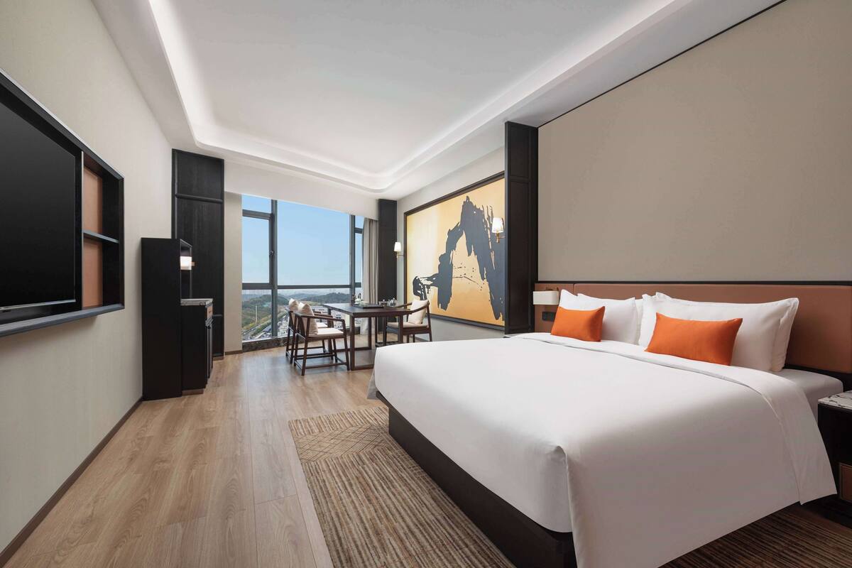 A hotel room with a large bed, a desk, and a view of the cityscape.
