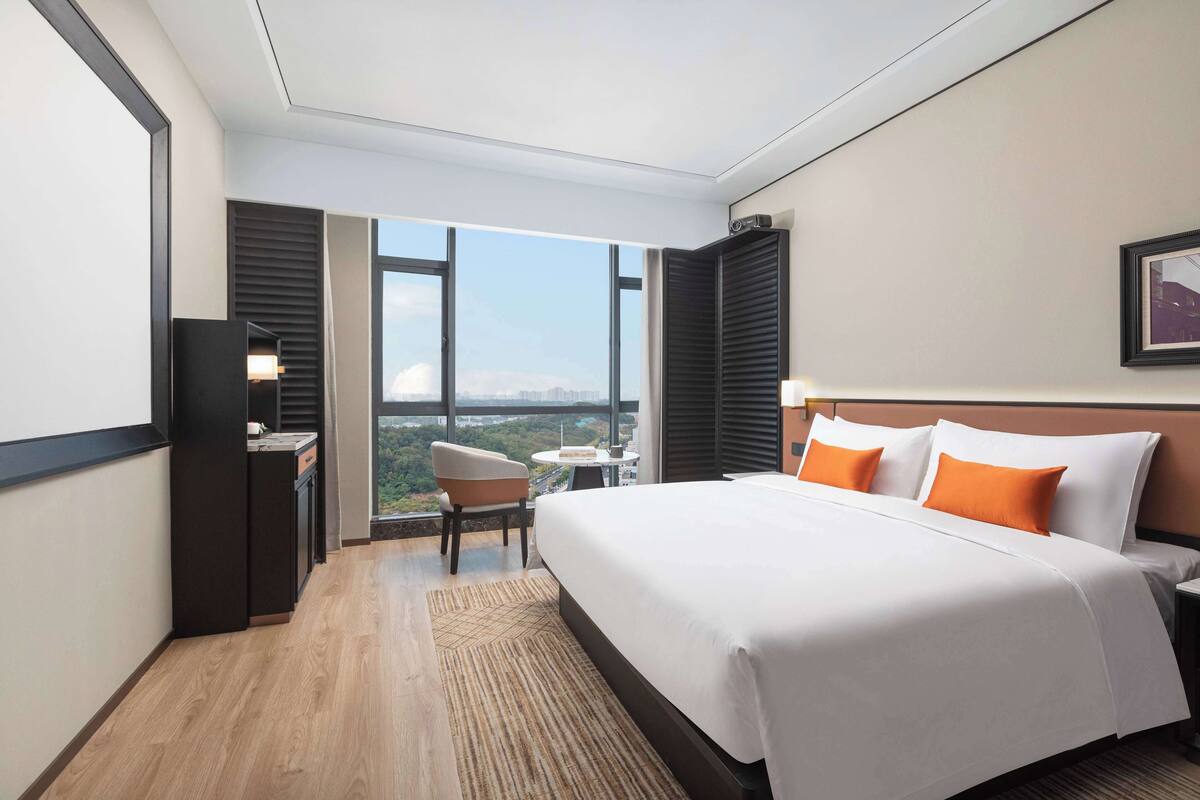 A hotel room with a large bed, a desk, a chair, and a view of the city.