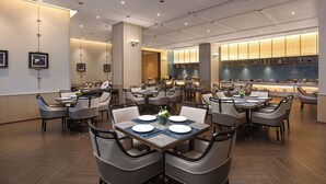 Un restaurante moderno con varias mesas y sillas, una zona de cocina con salpicadero de azulejos azules y cuadros en las paredes.