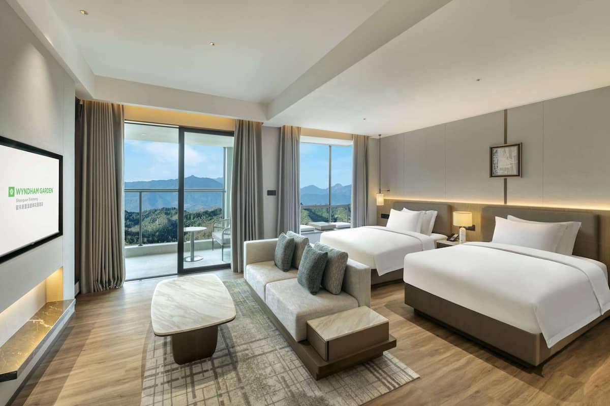 Een moderne hotelkamer met een groot bed, een bank, een eettafeltje en een balkon met uitzicht op de bergen.