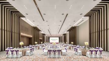 A large conference room with a stage at the front, rows of tables with chairs, and a carpeted floor.