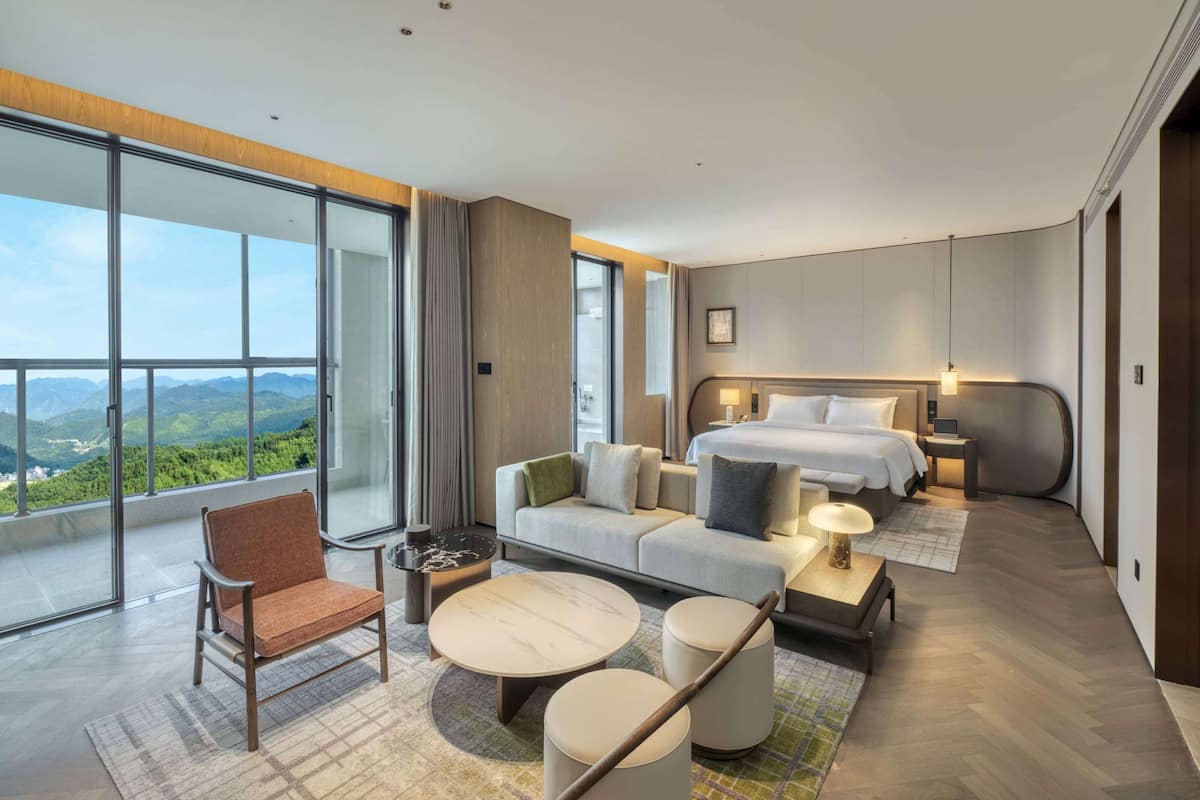 Een moderne hotelkamer met een ruim balkon, een bed, een sofa, een salontafel en een stoel.