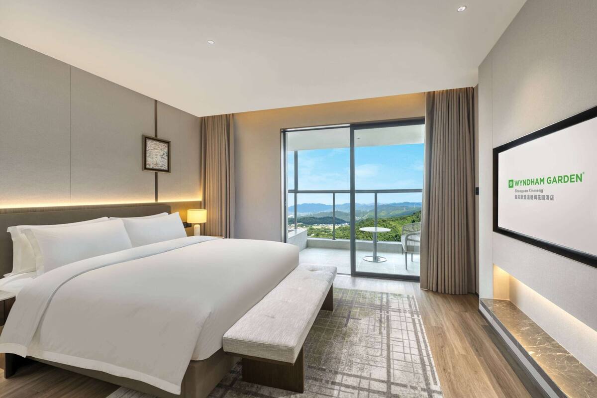 Een moderne hotelkamer met een groot bed, een bankje, uitzicht op de omgeving en een ingelijste foto aan de muur.
